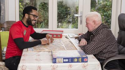 Thuishulp en klant die samen een spelletje spelen aan de eettafel 